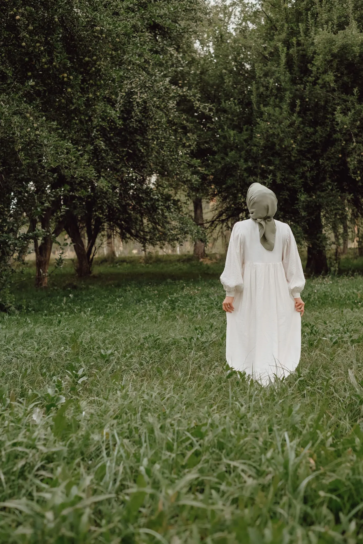 A woman in a long white dress and headscarf walking through a green park