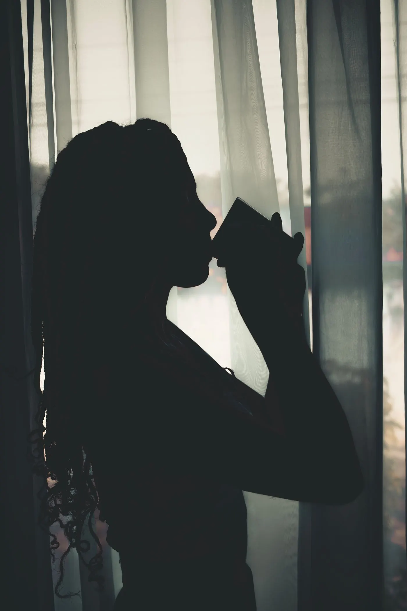 The silhouette of a woman sipping a drink by a window