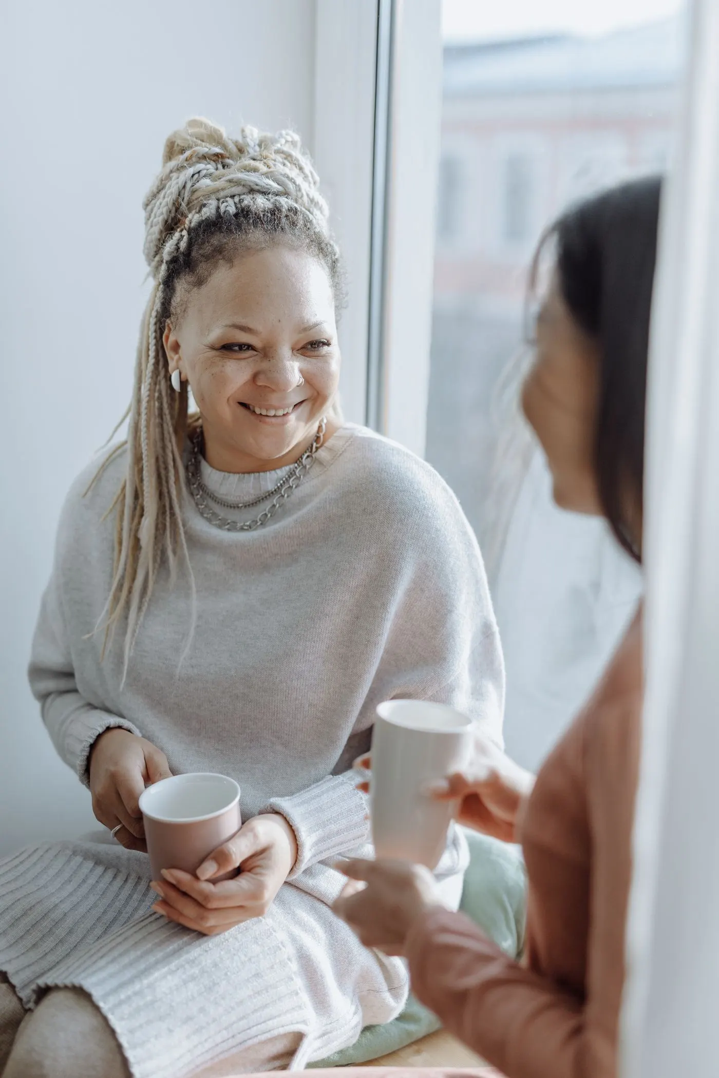 Two women talking over cups of tea at a sunny window