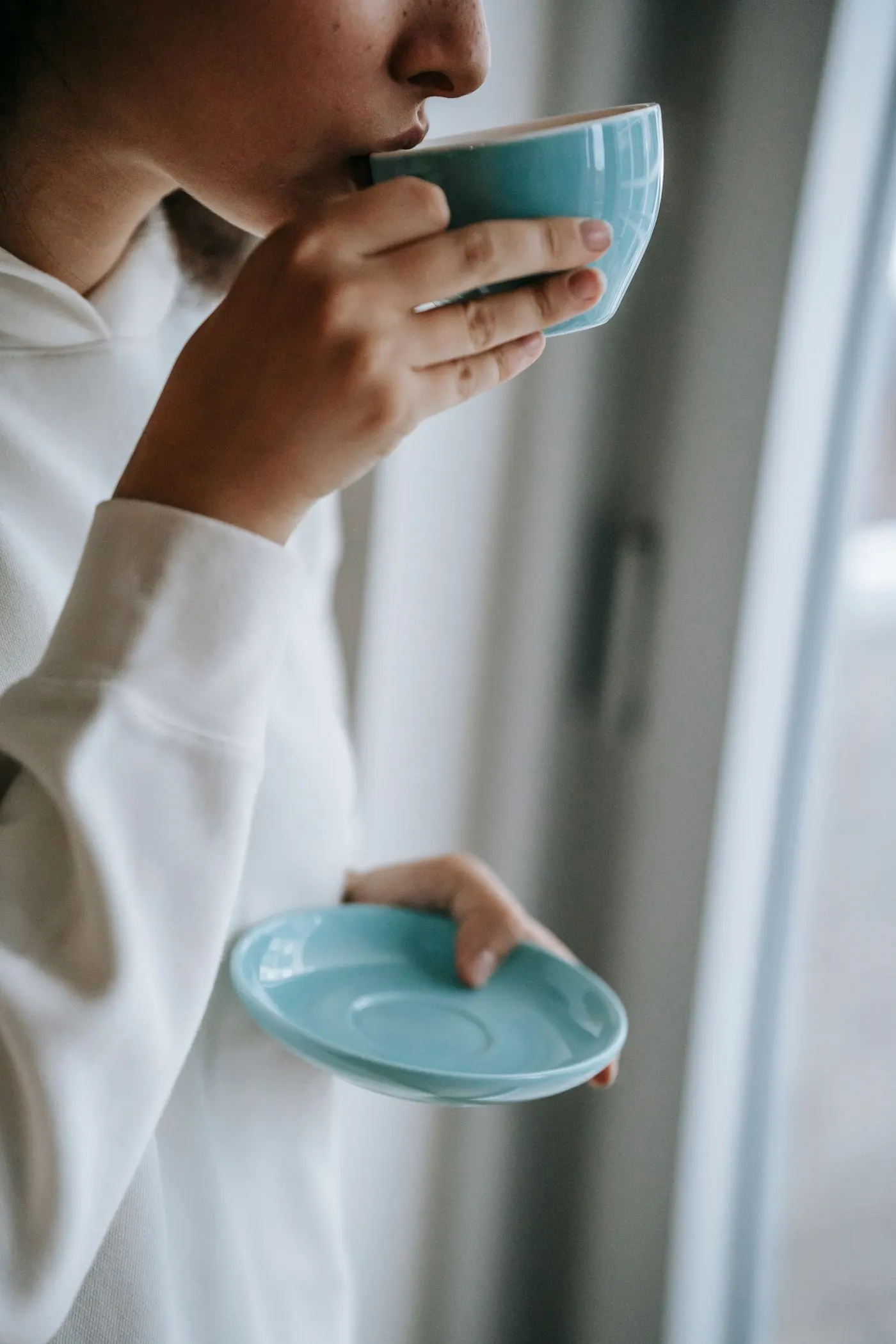 Hands holding a cup of tea by a sunny window